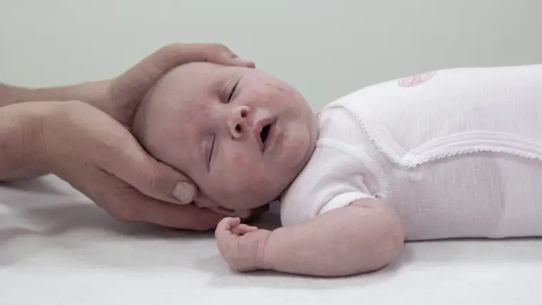 Pasgeboren baby op de behandelbank, een hand ondersteunt het hoofdje
